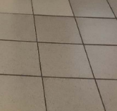 This is a tiled floor with a classic stone texture. It features a light beige color and the grout lines are darker and rougher.